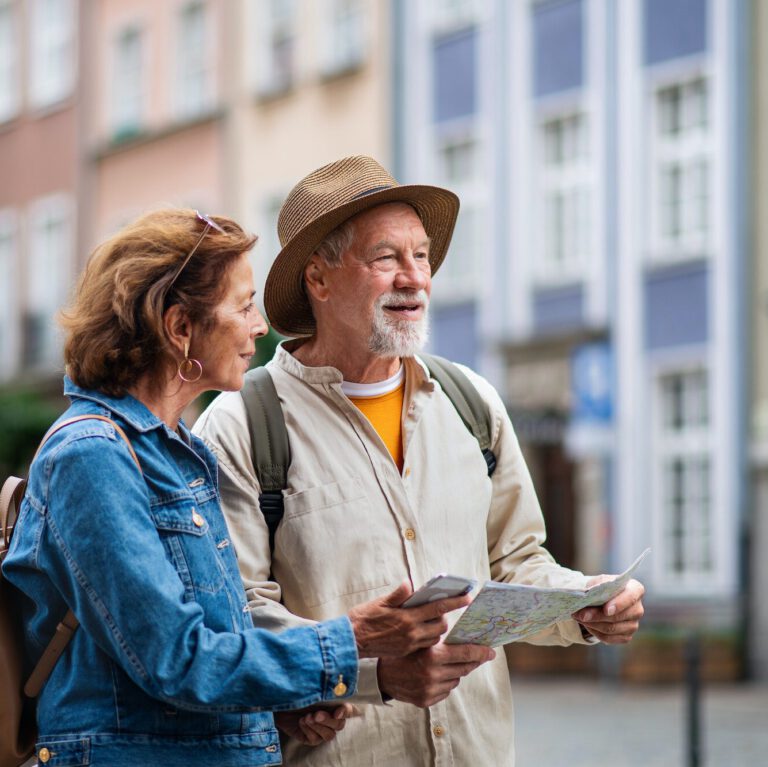 Portrait of happy senior couple tourists using map and smartphone outdoors in town street